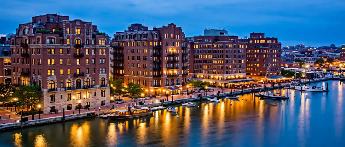 Baltimore Inner Harbor waterfront hotels at dusk with brick historic buildings, harbor boats, and warm evening lights
